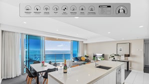 Quarto de hotel moderno com ampla área de jantar, cozinha e vista para o oceano.