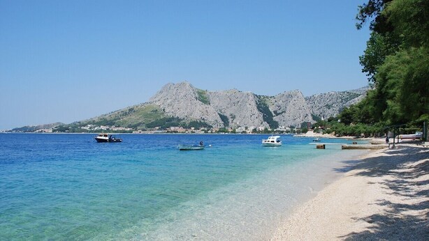 A beach with clear water, boats, and a mountainous backdrop. - Completely renovated small stone house with sea view near Split (Lokva Rogoznica)