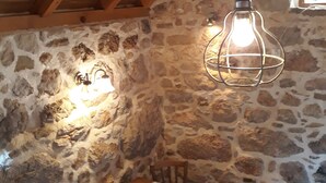 A rustic interior with a stone wall, wooden ceiling beams, a table with a white tablecloth, and a hanging light fixture. - Completely renovated small stone house with sea view near Split (Lokva Rogoznica)