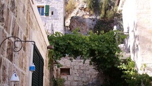 A narrow stone staircase leading up to a building with a tiled roof, surrounded by greenery and stone walls. - Completely renovated small stone house with sea view near Split (Lokva Rogoznica)