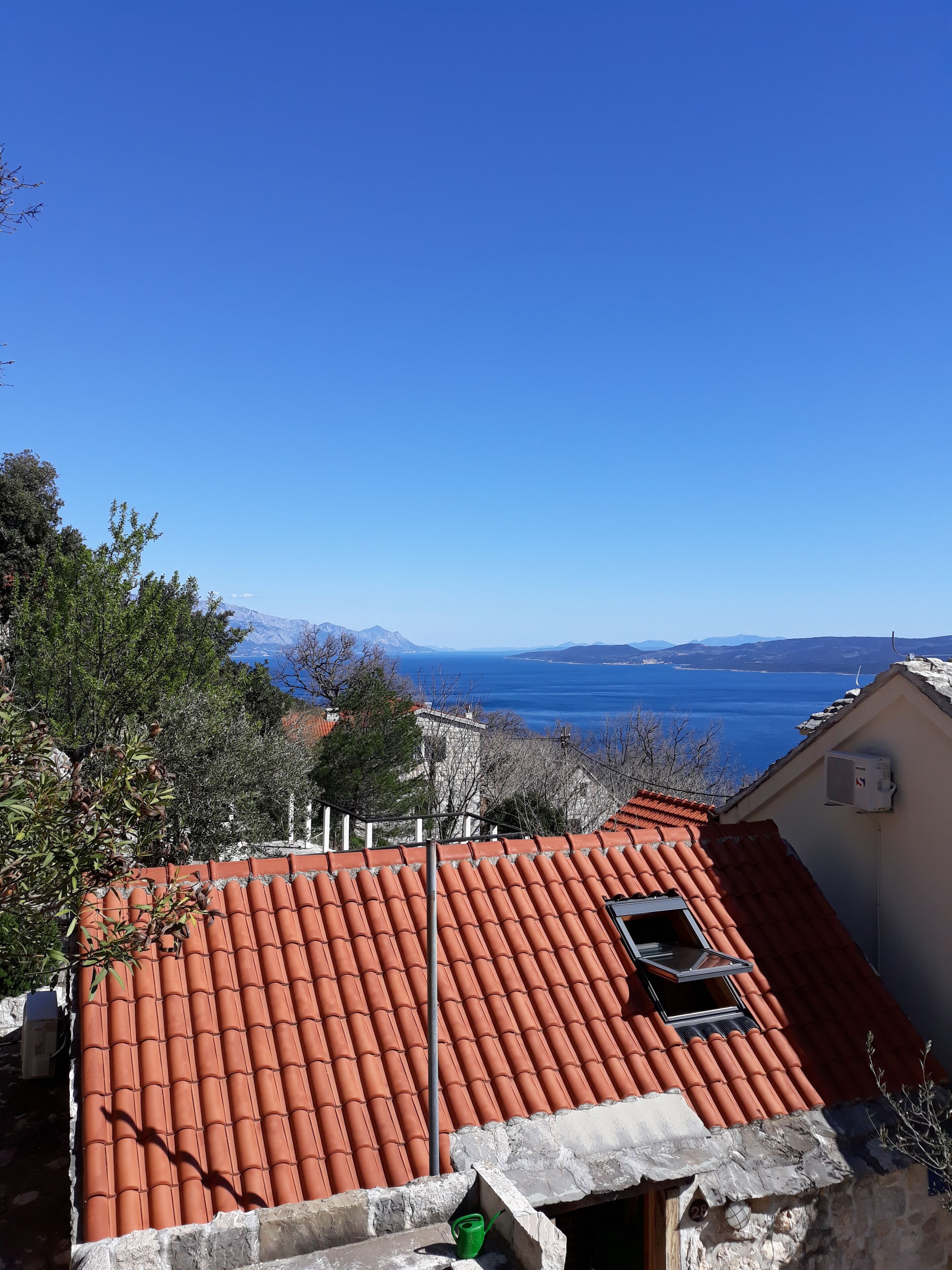 Un bâtiment doté d’un toit recouvert de tuiles rouges, d’une petite lucarne et offrant une vue sur la mer et les montagnes en arrière-plan.