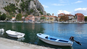 A waterfront with boats docked, buildings with red roofs, and a rocky cliff in the background. - Completely renovated small stone house with sea view near Split (Lokva Rogoznica)