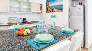 Une cuisine moderne dotée de plans de travail en granit, d’un réfrigérateur et d’un coin repas avec une table dressée pour deux personnes.