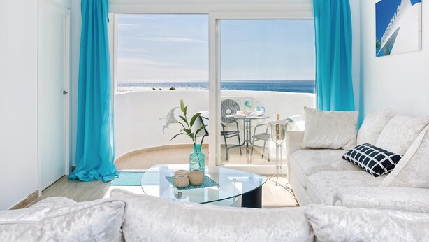 Une pièce avec une table en verre, un canapé blanc et une vue sur la plage.