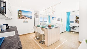 Une cuisine moderne dotée d’un îlot central, de meubles blancs et offrant une vue sur l’océan.