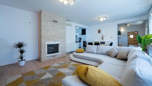 A modern living room with a fireplace, a sofa, a dining area, and a kitchen in the background. - Gorgeous home in Susnjevica (Susnjevica)