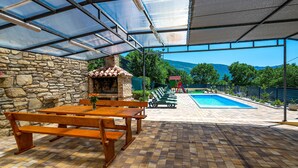 A covered patio with a stone wall, a brick fireplace, a pool, and outdoor furniture. - Gorgeous home in Susnjevica (Susnjevica)
