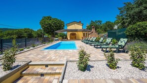 A pool area with a clear blue pool, lounge chairs, and a building with a yellow facade. - Gorgeous home in Susnjevica (Susnjevica)
