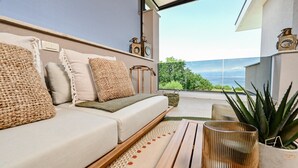 Ein modernes Wohnzimmer mit einer Couch, Kissen, einem Holztisch und Blick auf das Meer.