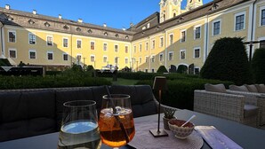 A table with two wine glasses and a bowl of fruit, set against a backdrop of a historic building with a clock tower. - Live like a king - maisonette apartment in a castle hotel (Mondsee)