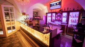 A bar area with a marble counter, shelves of liquor bottles, and a television screen displaying a logo. - Live like a king - maisonette apartment in a castle hotel (Mondsee)