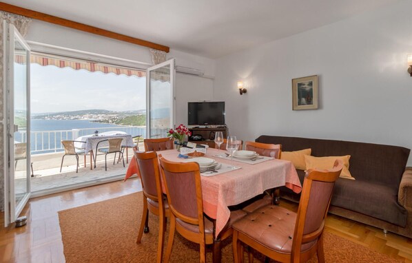 Un comedor con una mesa preparada para cuatro personas, un sofá y una televisión en una habitación con vista al mar.
