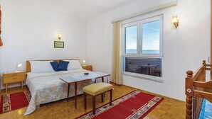 Un dormitorio con cama, mesitas de noche, una mesa con mantel de encaje, una silla, una ventana con vistas y una silla de madera en la esquina.