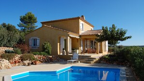 Une maison à deux étages avec une piscine, un espace salon extérieur et un mur en pierre.