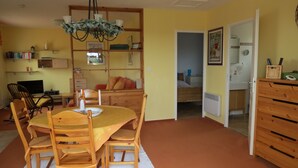 Une pièce chaleureuse avec une table à manger en bois, des chaises, une bibliothèque, un lit et une salle de bain visible à travers une porte ouverte.