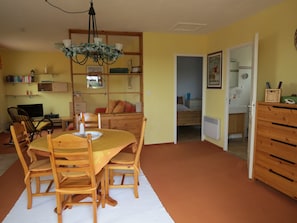 A cozy room with a wooden dining table, chairs, a bookshelf, a bed, and a bathroom visible through an open door. - Apartment in villa with pool, oasis of relaxation, view of mountains (Seillons-Source-D'argens)