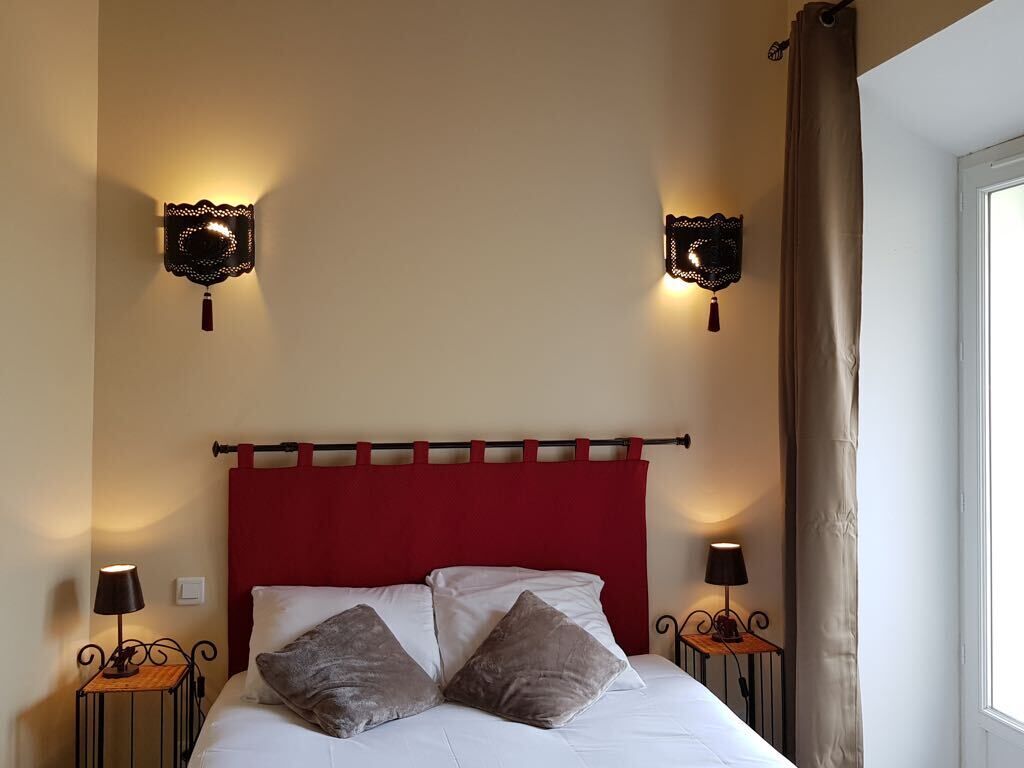 Un lit avec une tête de lit rouge, deux appliques murales et une fenêtre avec un rideau.