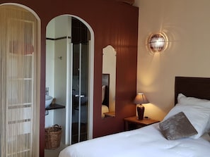 Hotellihuone, jossa on sänky, yöpöytä lampun kanssa, peili ja vaatekaappi.