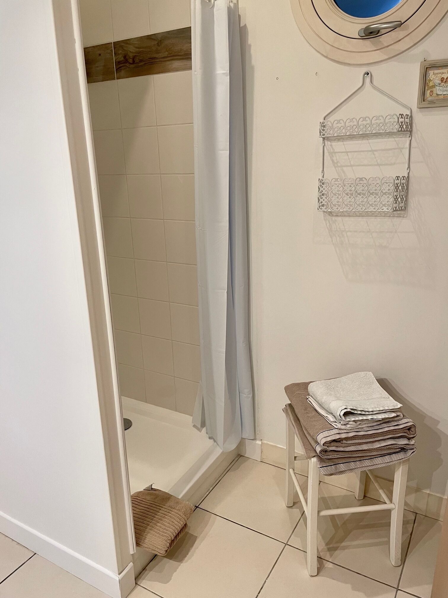 A bathroom with a shower, a towel rack with a folded towel, and a small stool.