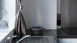 Uma cozinha moderna com uma pia de aço inoxidável, uma janela com cortinas e uma cesta sobre o balcão.
