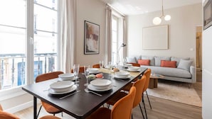 Een eetgedeelte met een tafel voor vier personen, een bank en een stadszicht door grote ramen.