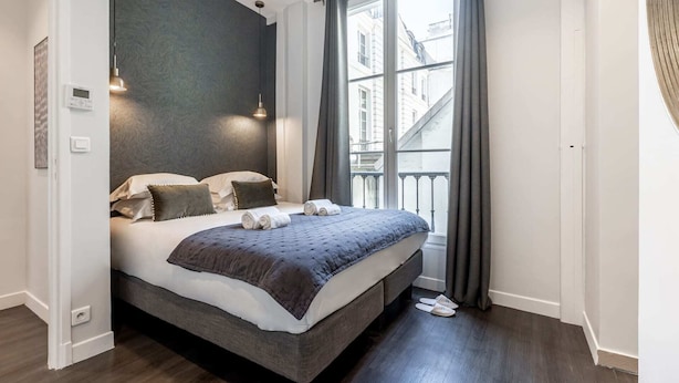 Een moderne slaapkamer met een groot bed, een donkere accentmuur en uitzicht op gebouwen door een raam.