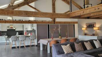Een moderne keuken met witte kasten, een eethoek met een tafel en stoelen, en een woonkamer met een bank en kussens.