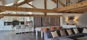 A modern kitchen with white cabinets, a dining area with a table and chairs, and a living room with a sofa and cushions.