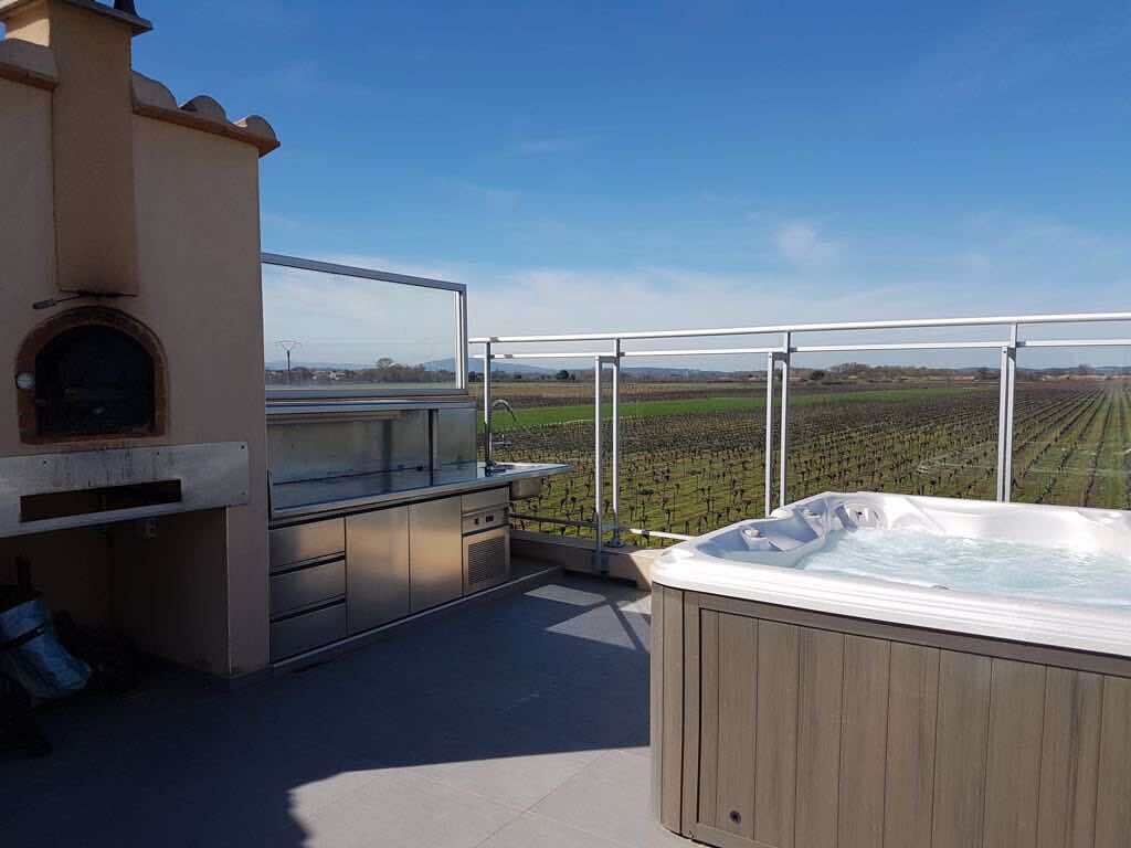 Een terras op het dak met een jacuzzi, een barbecuehoek en uitzicht op een wijngaard.