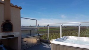 Terraza en la azotea con jacuzzi, zona de barbacoa y vistas a un viñedo.