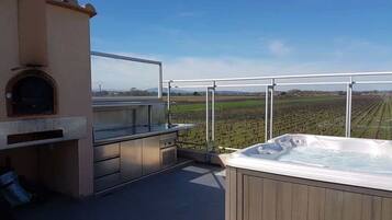 Een terras op het dak met een jacuzzi, een barbecuehoek en uitzicht op een wijngaard.