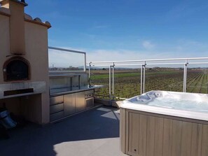 A rooftop terrace with a hot tub, a barbecue area, and a view of a vineyard.