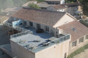 A two-story building with a flat roof, a balcony with glass railings, and a patio area with outdoor furniture.