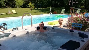 Un bain à remous dans un jardin, avec une piscine, entouré de verdure et de mobilier d’extérieur.