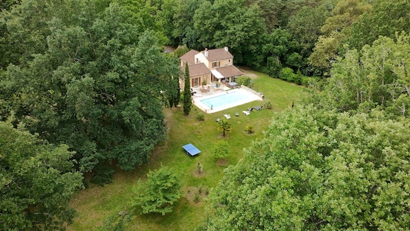 Une vue aérienne d’une maison entourée d’une forêt dense, avec une piscine et du mobilier d’extérieur.