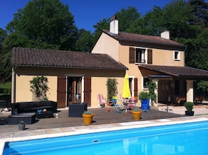 Une maison à deux étages avec une piscine, du mobilier d’extérieur et des plantes en pot.