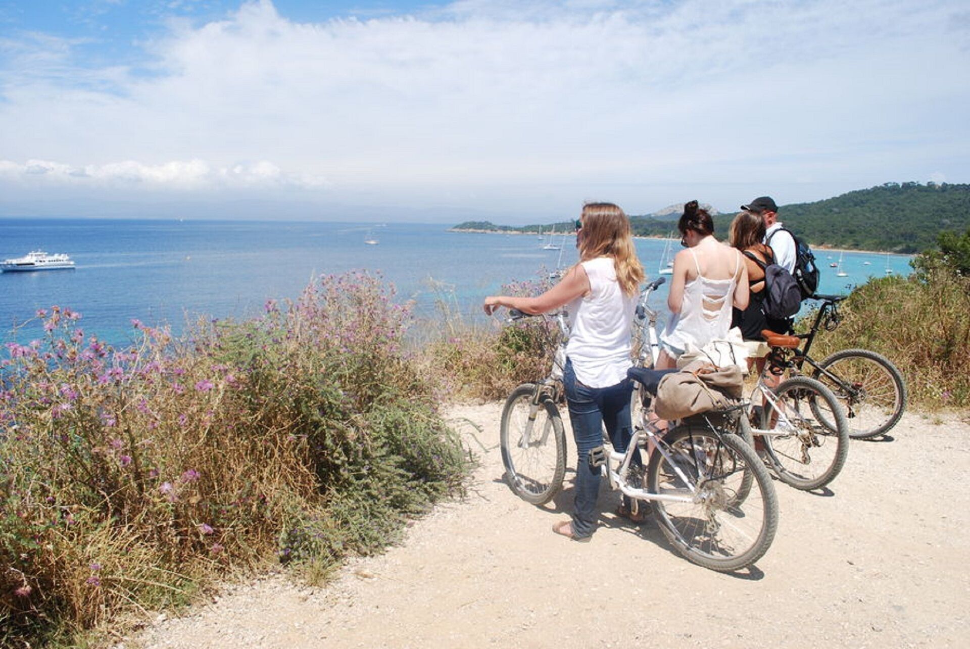 Un gruppo di persone in bicicletta con vista su una zona costiera e imbarcazioni in acqua.