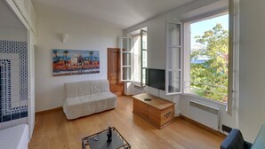 A living room with a white sofa, a wooden cabinet, a TV, and a painting on the wall.