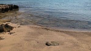 A beach with clear water, rocky shoreline, and distant mountains.