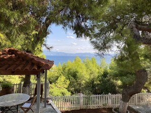 A patio with a table and chairs, a pergola, a white picket fence, and a view of the sea and mountains. - Great beachfront villa with private pool and garden for 10/12 people (Theologos)
