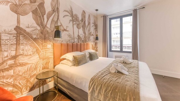 A bedroom with a bed, a nightstand, a wall mural, a window with curtains, and a balcony view. - Sweett | Troyon - Three Bedroom Apartment, Sleeps 6 (Paris)