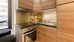 A compact kitchen with wooden cabinetry, a stainless steel sink, and a built-in oven. - Sweett | Troyon - Three Bedroom Apartment, Sleeps 6 (Paris)