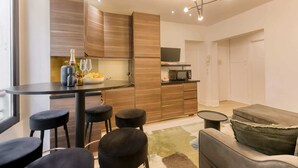 A modern kitchen with wooden cabinets, a dining area with stools, a sofa, and a TV. - Sweett | Troyon - Three Bedroom Apartment, Sleeps 6 (Paris)