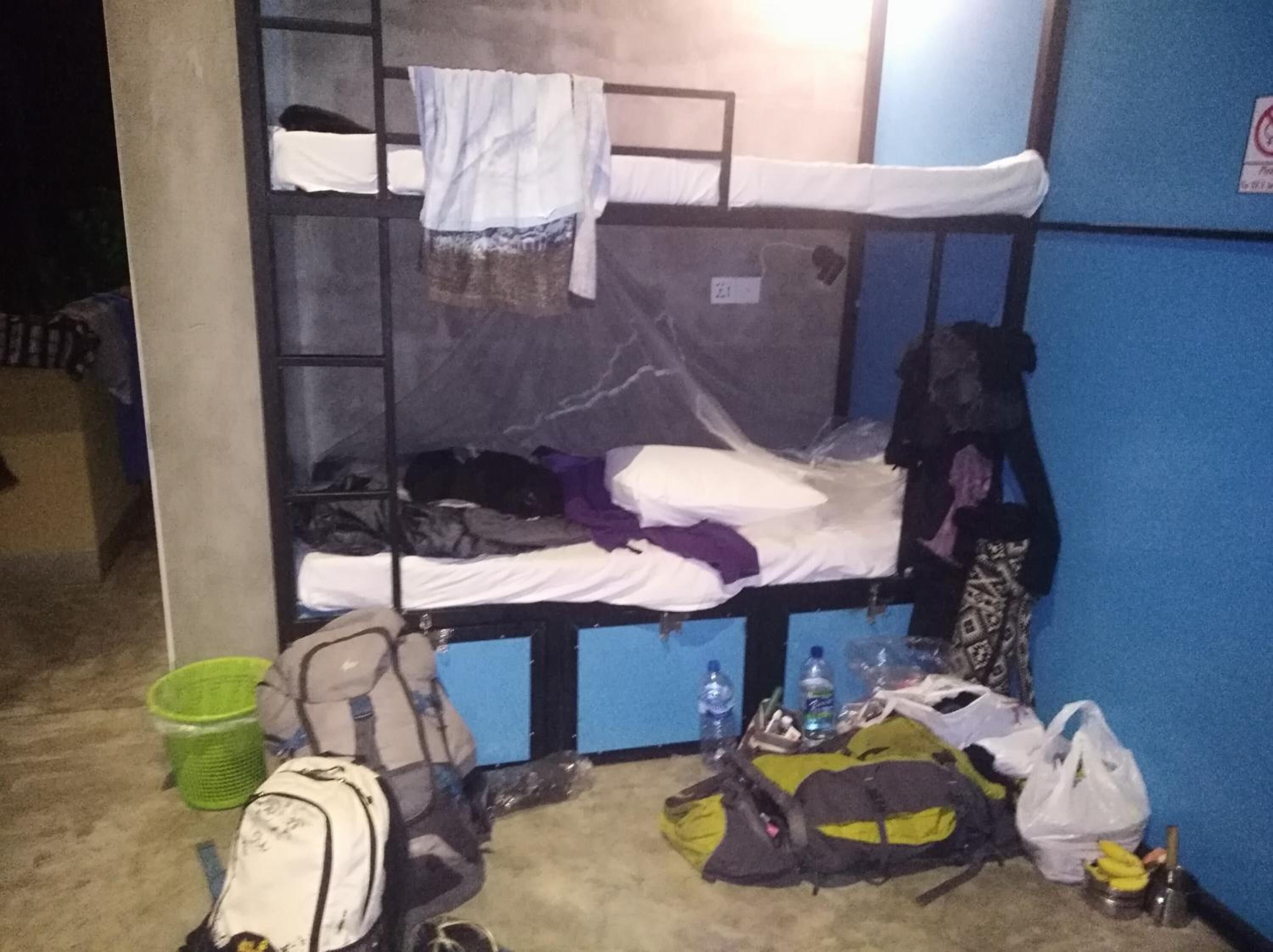 A bunk bed room with a blue wall, a green basket, and various bags and bottles on the floor.