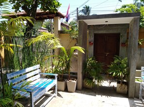 A courtyard with a wooden bench, potted plants, and a concrete structure with a door.
