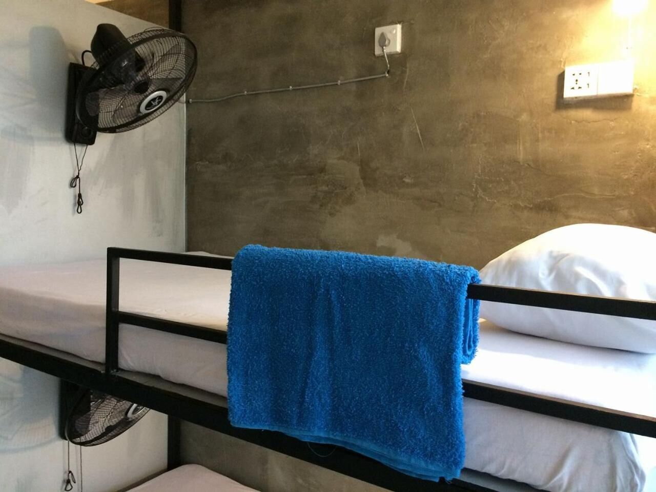 A bunk bed with a blue towel, a wall-mounted fan, and a power outlet.