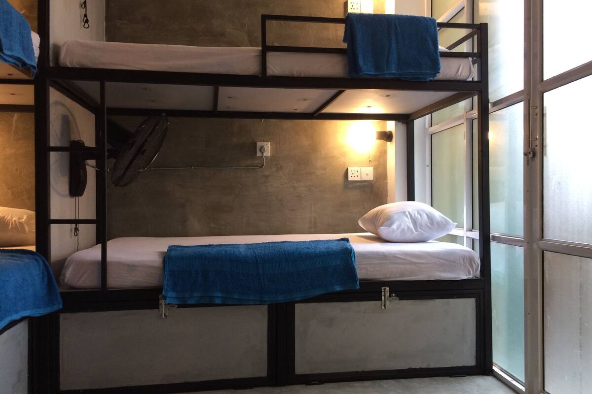 A bunk bed room with a window, a wall-mounted fan, and a power outlet.