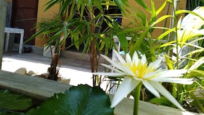 A courtyard with a yellow building, a wooden table, and various plants including a white flower. - Cycling Hostel Sri Lanka (Unawatuna)