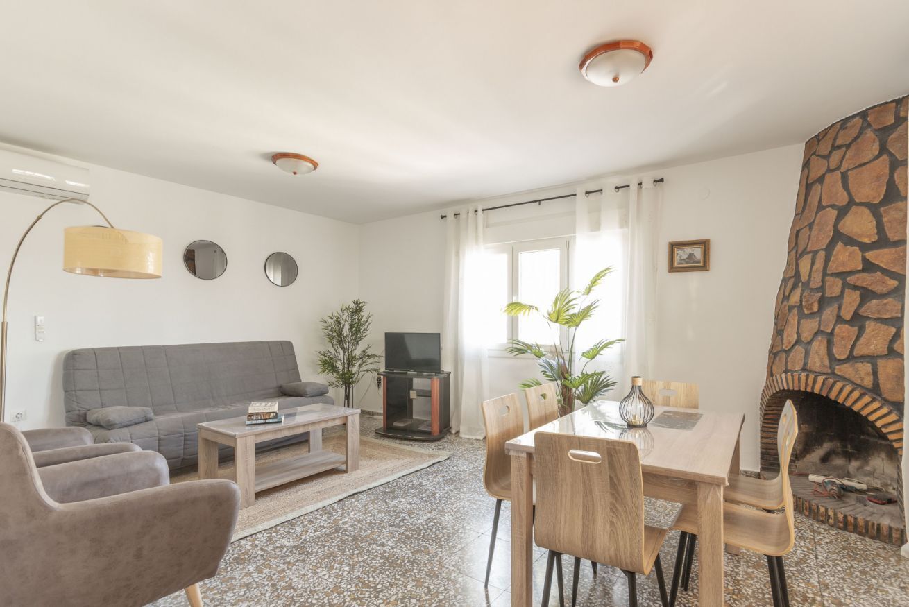 Una sala de estar con chimenea de piedra, un sofá gris, una mesa de centro y una mesa de comedor con sillas.