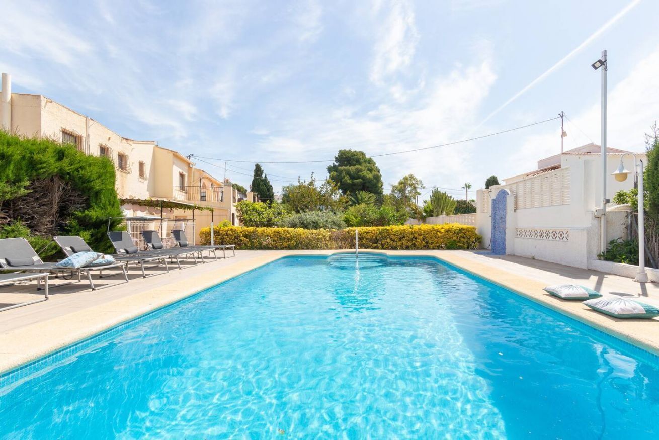 Une piscine rectangulaire à l’eau d’un bleu cristallin, entourée de chaises longues et d’une haie basse.